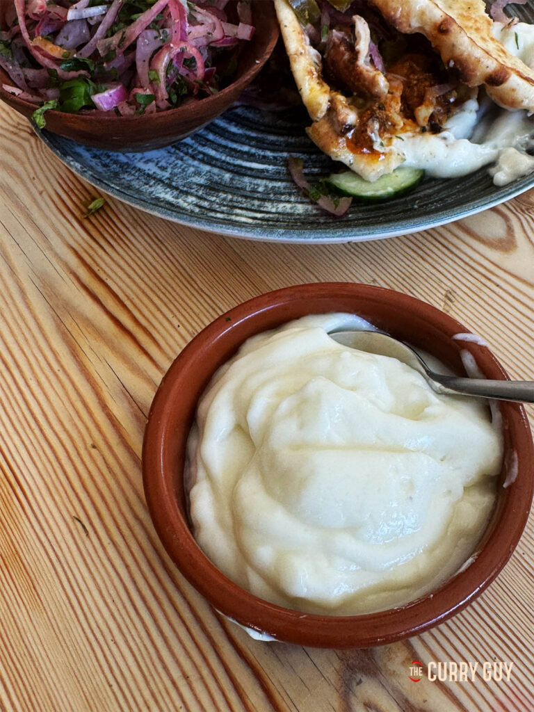 Garlic sauce with a kebab in the background.