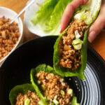 Pork lettuce wraps. Two on a plate and one being held ready to eat.