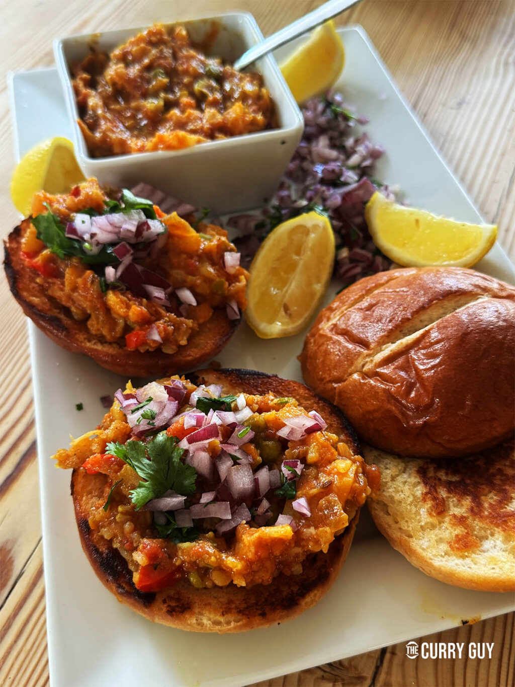 Pav Bhaji served on a plate with lemons and chopped onion garnish.